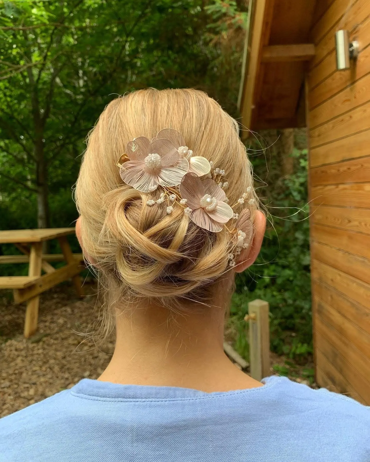 Blonde updo of loose pinned curls decorated with blush pink fabric flowers and pearls, outdoors