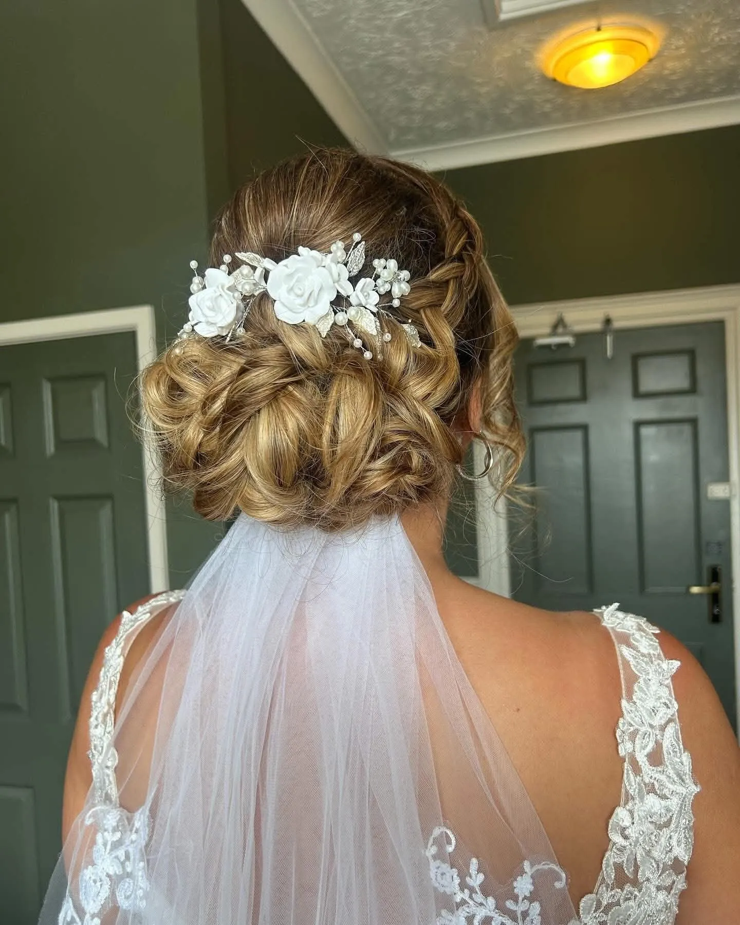 Back view of a bride with a textured low updo, a white flower and pearl comb and a tulle veil beneath it