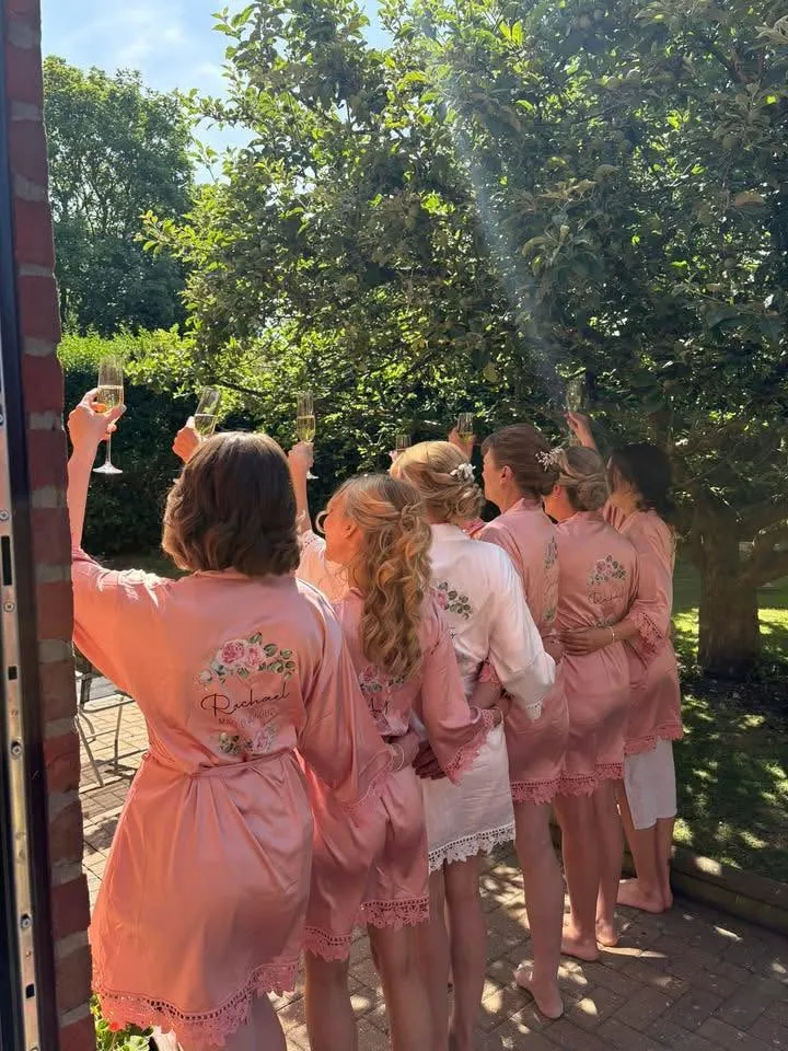 A bridal party in blush robes raising champagne flutes in a garden, hair styled and ready.