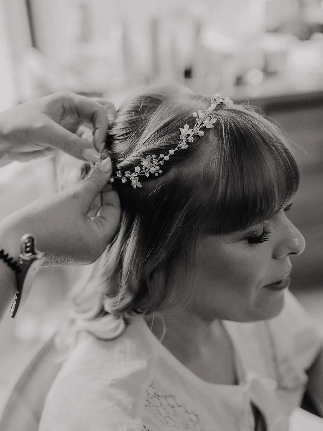 Hands pinning a pearl and crystal hair vine into a bride's soft half-up style.
