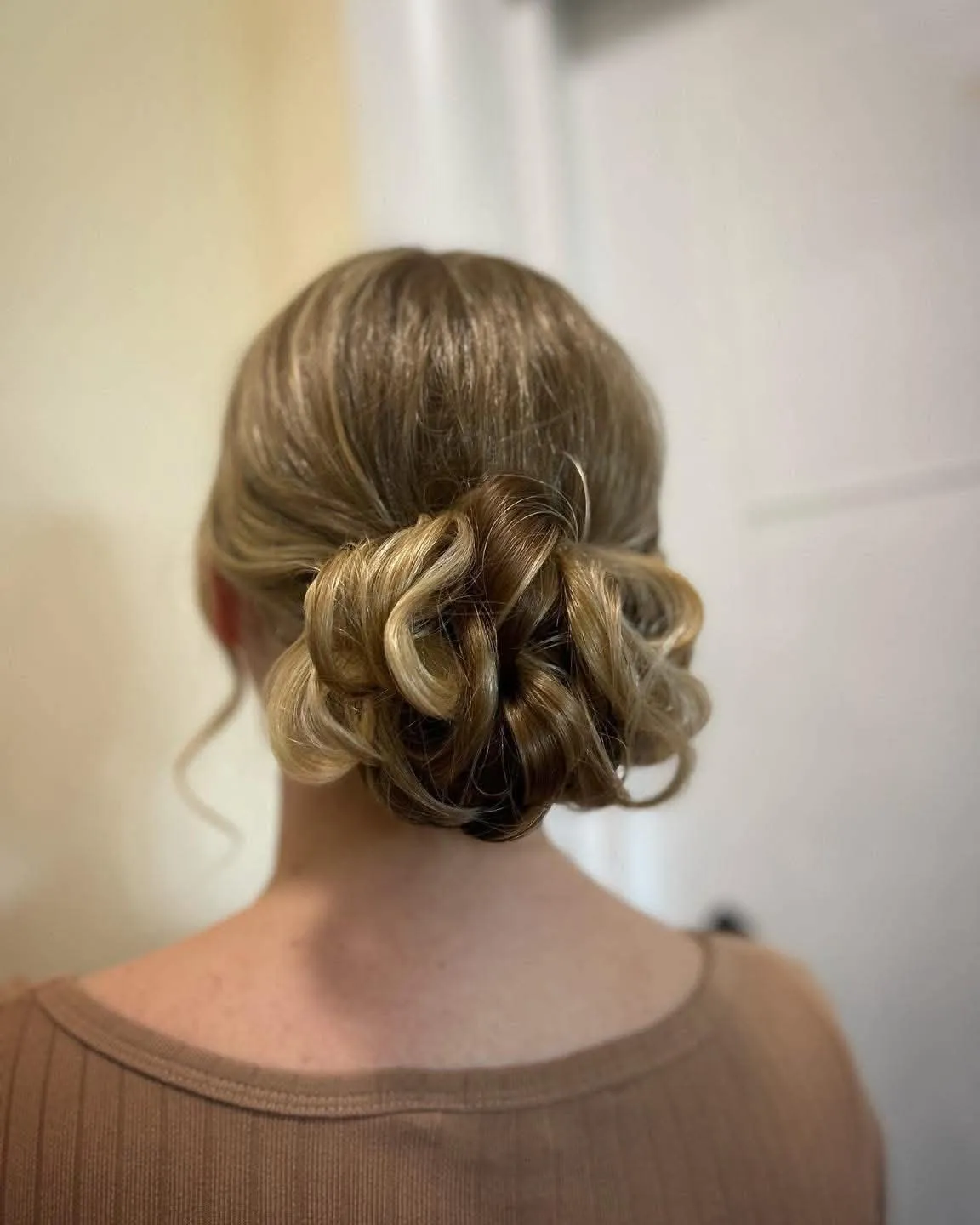 Low bun of soft gathered curls in highlighted blonde hair, seen from behind
