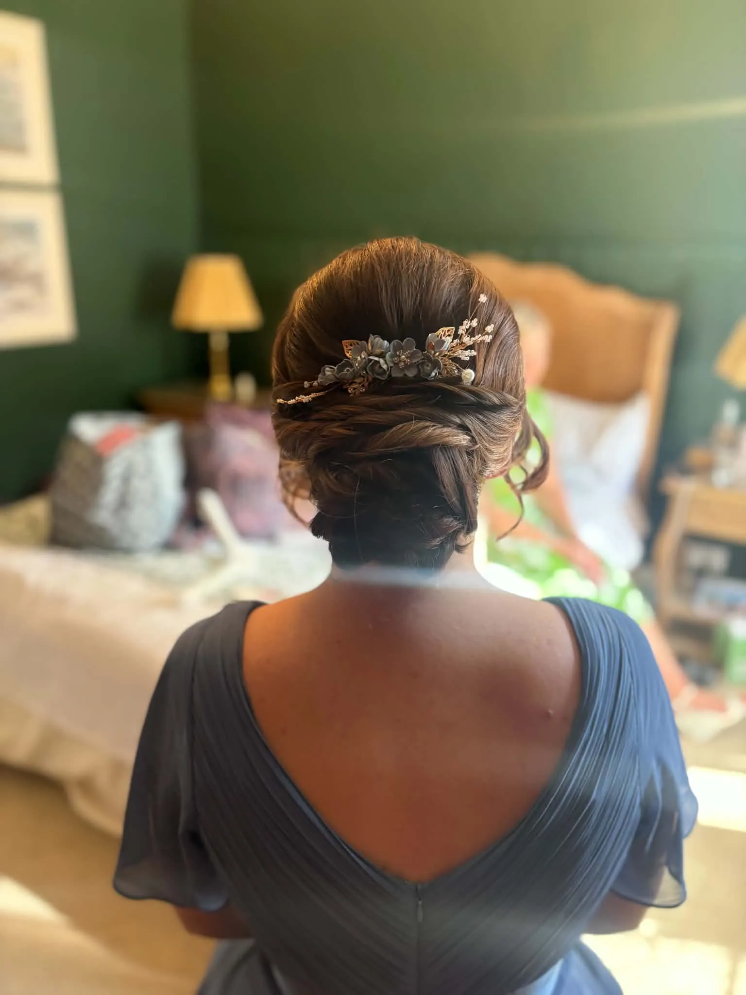 Bridesmaid in a grey-blue dress with a soft low updo and a leaf and pearl hairpiece, in a green bedroom