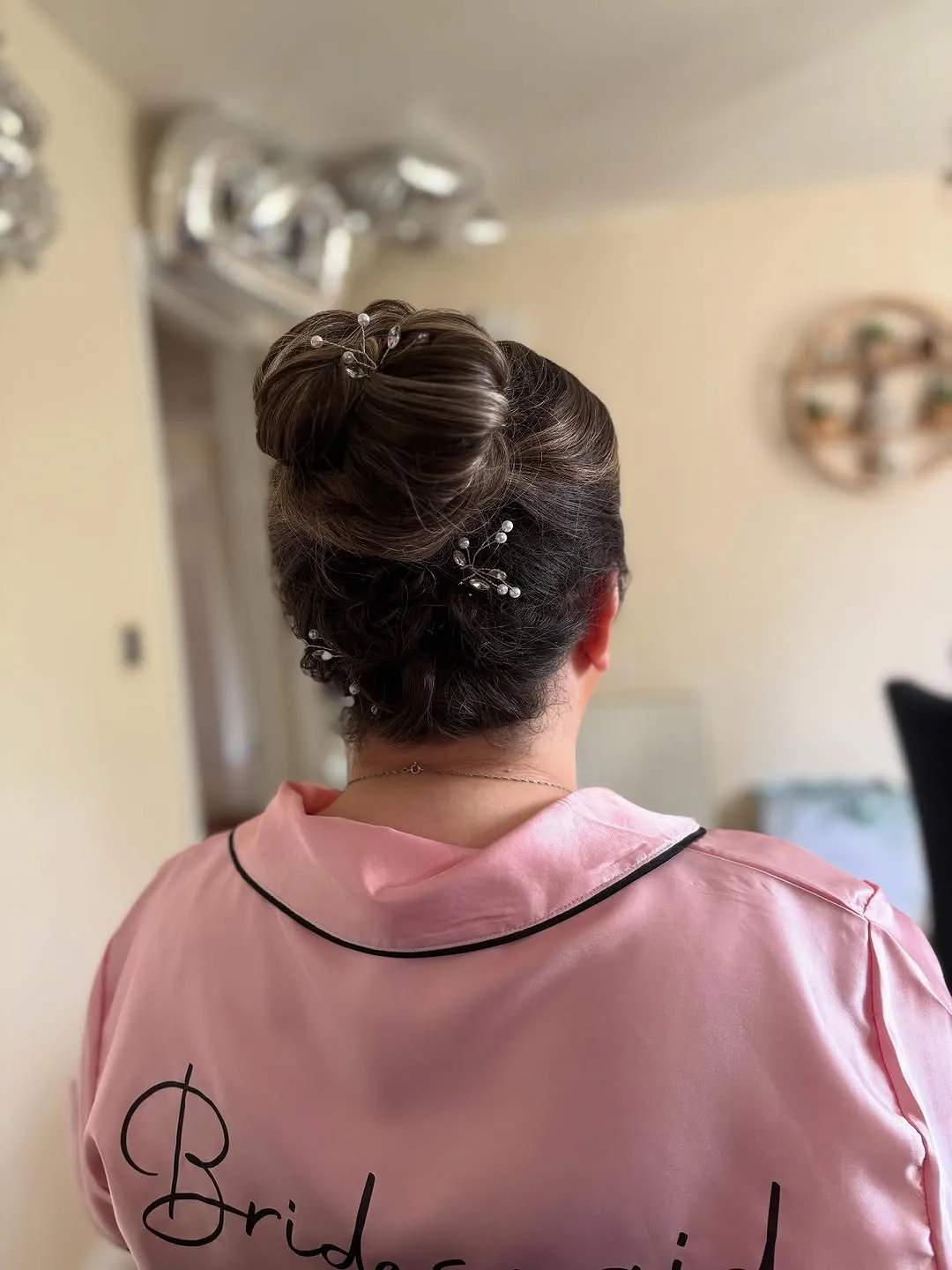 Sleek high bun set with crystal pins, worn with a pink bridesmaid robe.